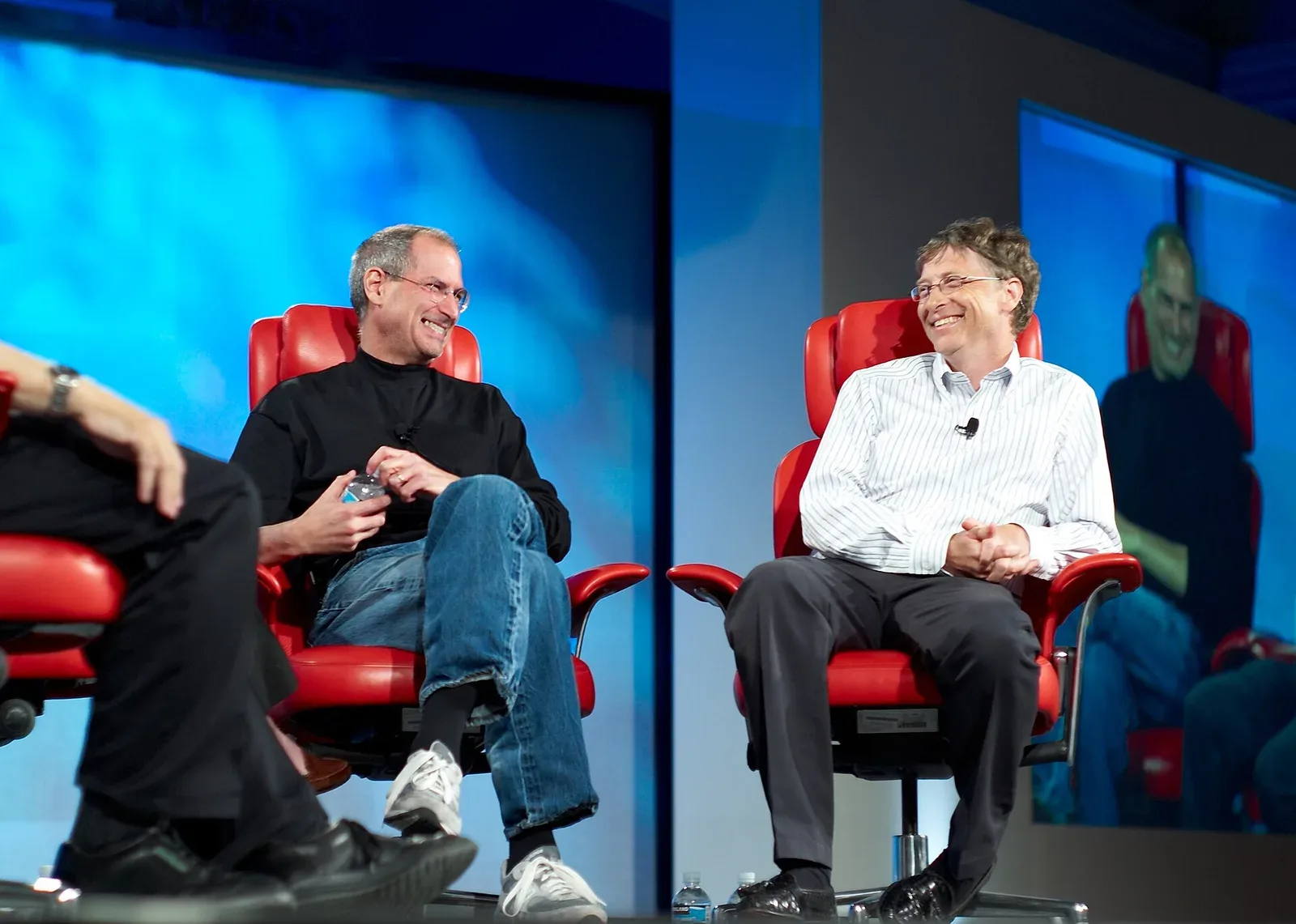 Bill Gates conversa con Steve Jobs sentados en sillas rojas durante una conferencia