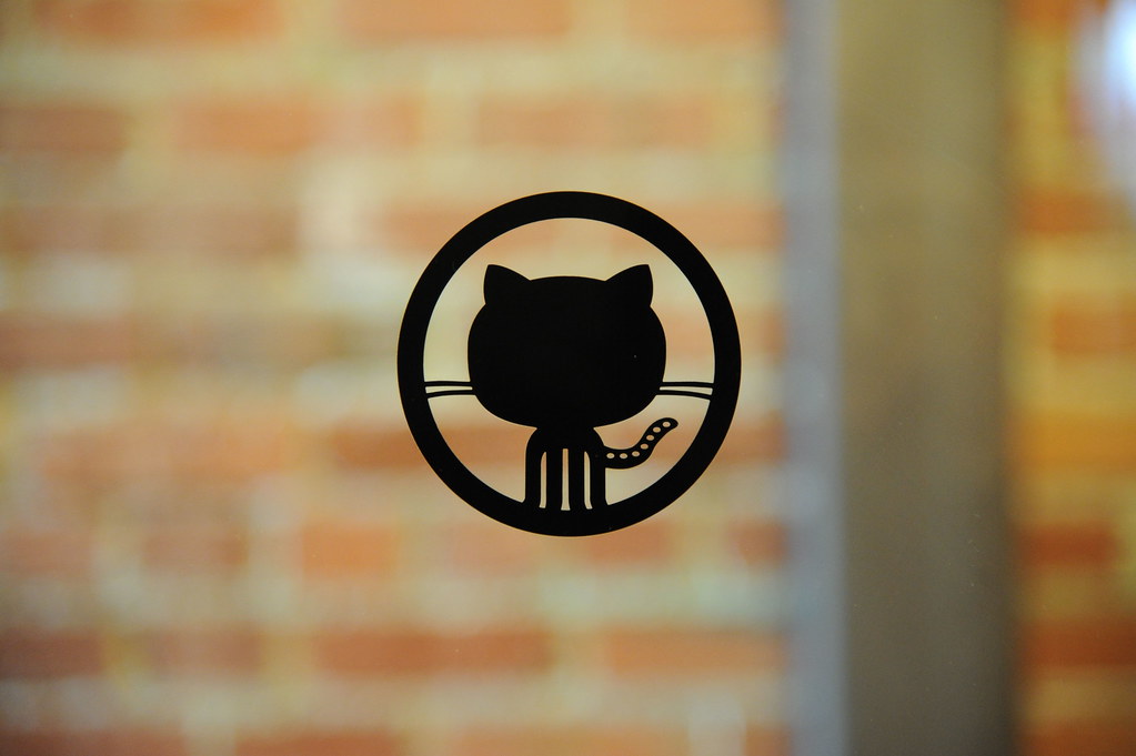 Logotipo de GitHub adherido a una puerta de vidrio, con fachada de ladrillo al fondo