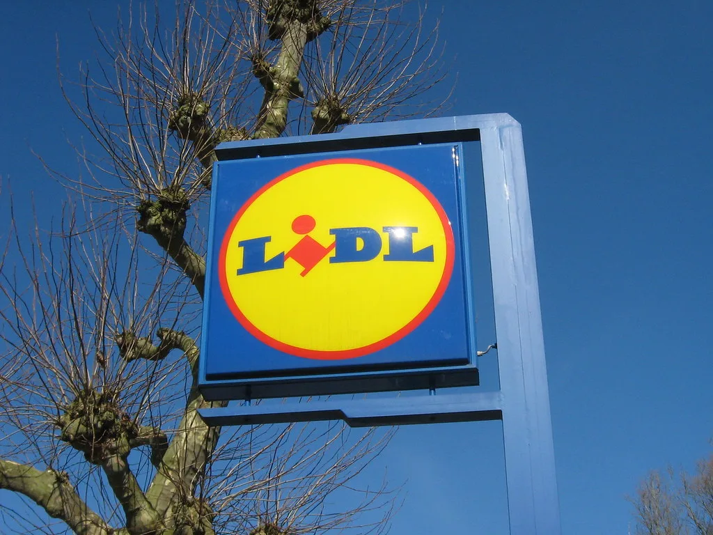 Cartel luminoso con el logotipo de Lidl junto a un árbol, cielo despejado