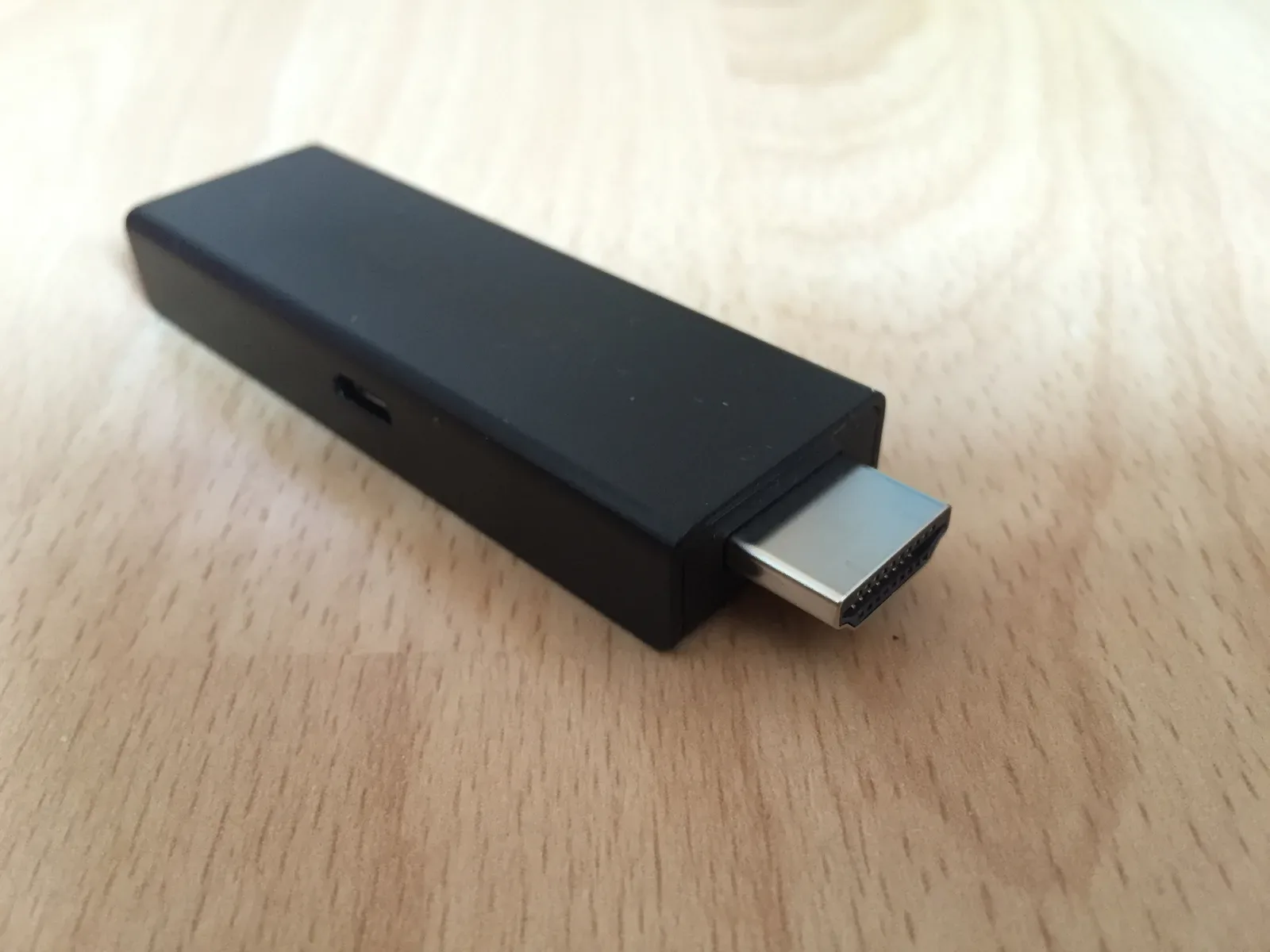 Dispositivo HDMI streaming negro con puerto USB, apoyado sobre mesa de madera