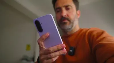 Un hombre observa la pantalla de un smartphone morado que sostiene con la mano.