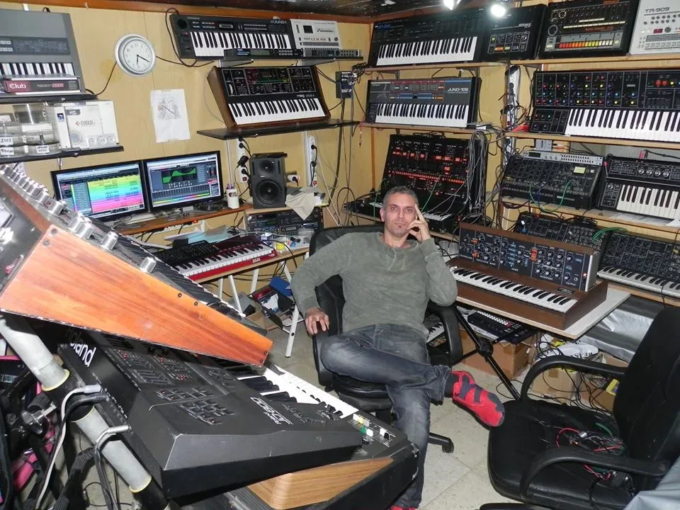 Hombre sentado en estudio con teclados y sintetizadores musicales