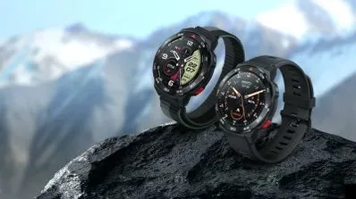 Dos relojes inteligentes negros colocados sobre una roca con montañas nevadas de fondo