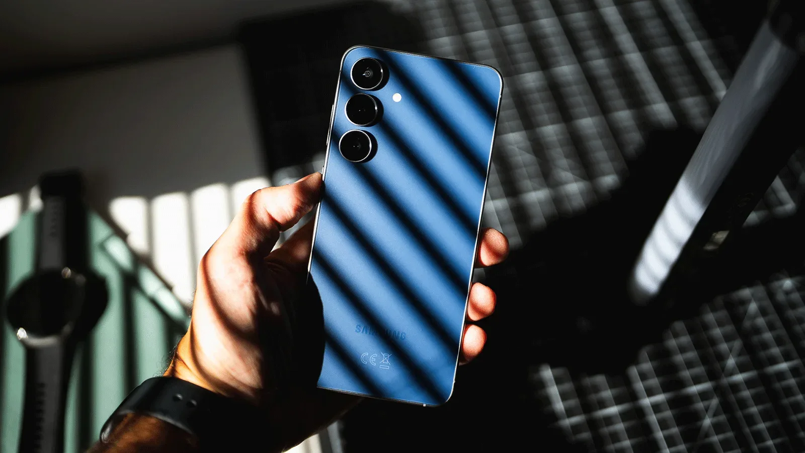 Una mano sostiene un smartphone Samsung en color azul con luz cenital