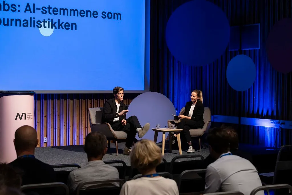 Dos ponentes conversan en un escenario bajo una pantalla sobre IA en periodismo