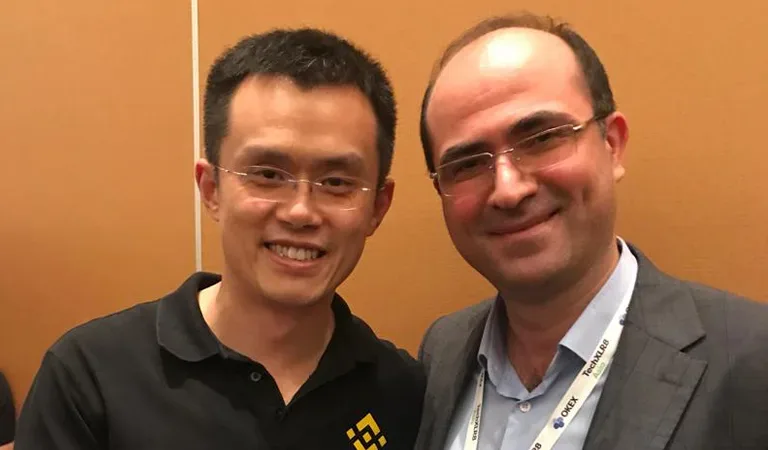 Dos hombres sonríen en un evento, uno con polo con logo de Binance