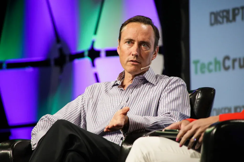 Hombre con micrófono de diadema conversa sentado en el escenario de TechCrunch Disrupt