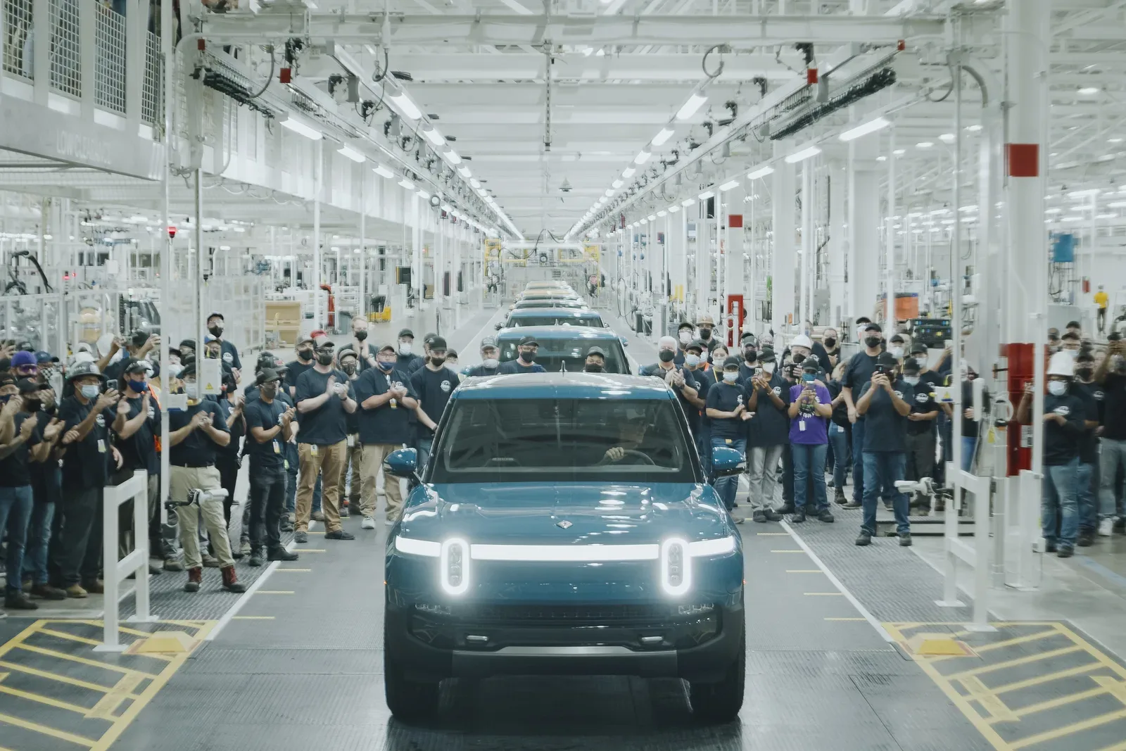 Trabajadores aplauden la salida de un vehículo eléctrico Rivian en planta de montaje