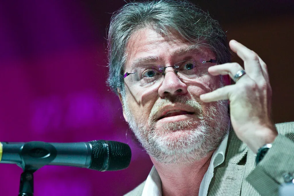 Un hombre con gafas gesticula mientras habla frente a un micrófono