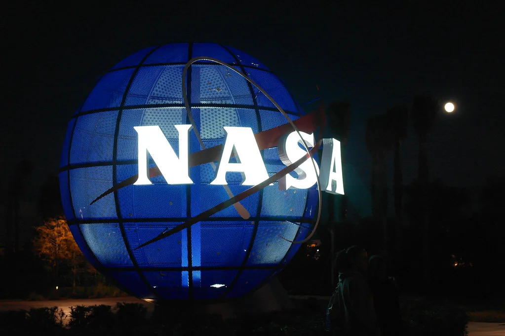 Escultura iluminada del logotipo de la NASA fotografiada de noche junto a palmeras