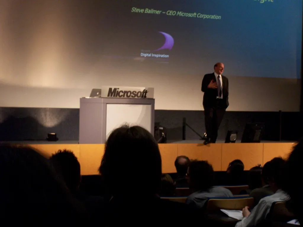 Hombre habla en un escenario junto a atril con el logo de Microsoft