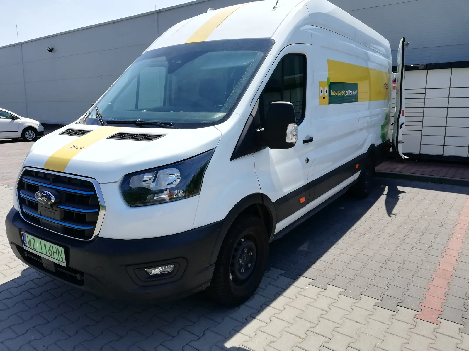 Furgoneta Ford blanca con logotipos amarillos y verdes estacionada junto a un almacén